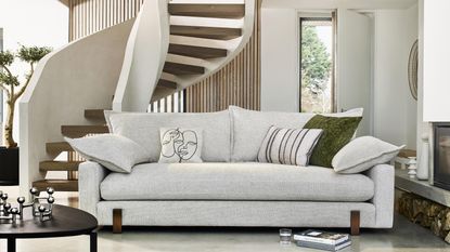 A modern living room with neutral upholstered sofa and sculptural staircase