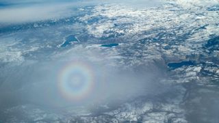 A circular rainbow glory in a cloud above a snowy landscape, taken from an airplane