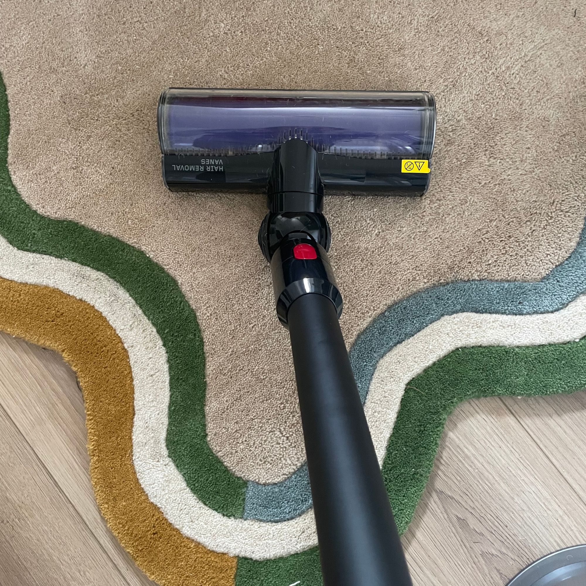 Using the Dyson V8 Cyclone to vacuum a cream rug with colourful edges