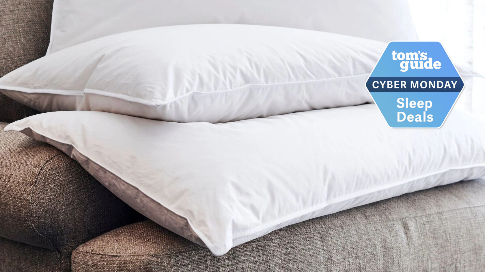 A stack of Westin Down pillows on a grey couch with TG Cyber Monday Sleep Deals badge on the right side