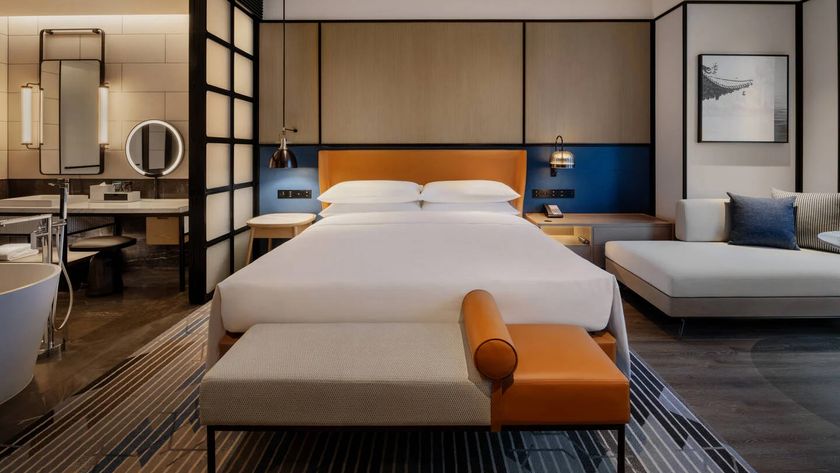 A Sheraton Mattress, bedding and pillows in a Sheraton hotel room. To the left, you can see the edges of the bathroom, to the right, a sitting area.