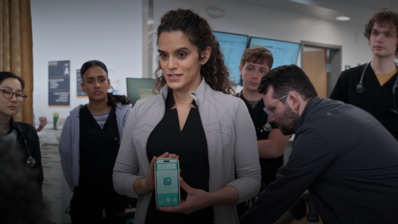 Sepideh Moafi holding a phone in front a group of doctors in The Pitt