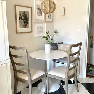 Round dining table in magnolia painted kitchen with checked black and white floors, small gallery wall and wooden chairs