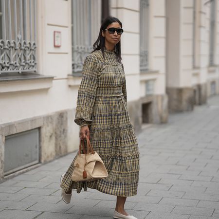 stylish woman wearing a full length gingham printed dress with flats and a raffia bag with sunglasses. 