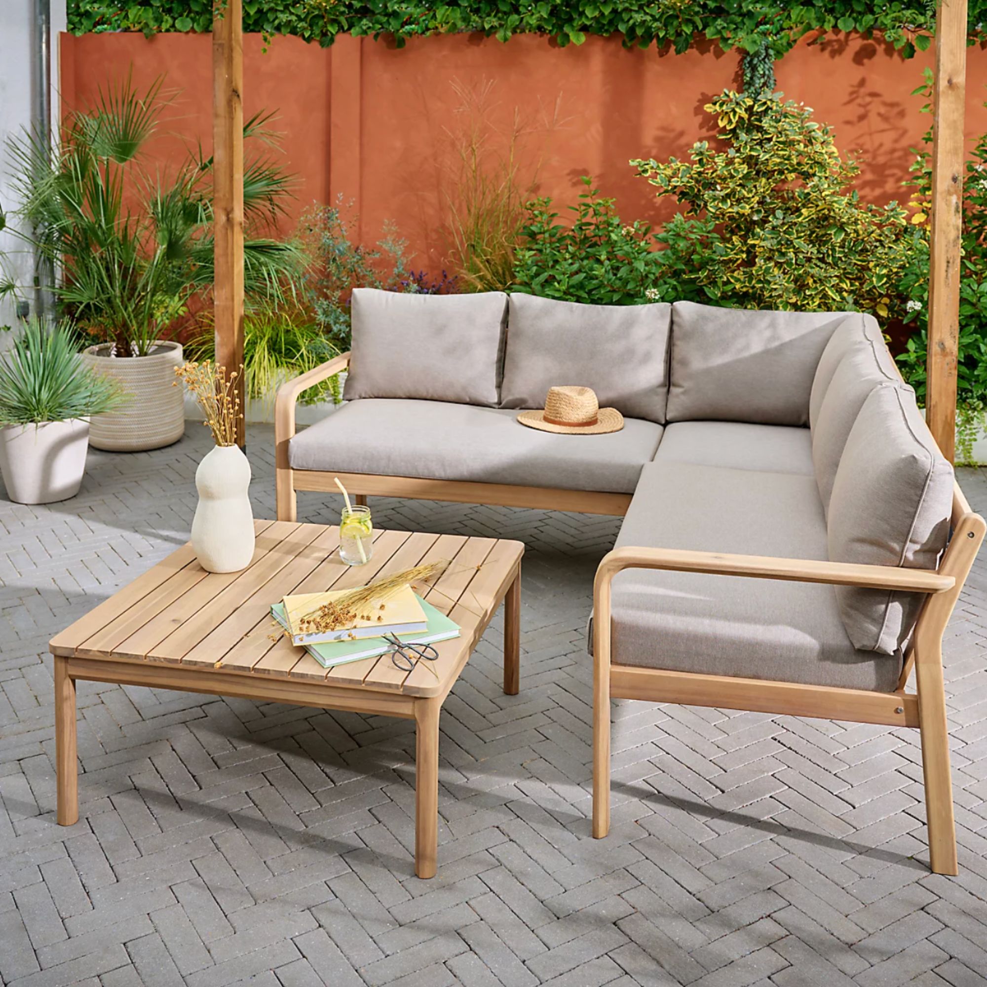 GoodHome Riveo Natural Wooden 5 Seater Modular corner Garden furniture set on patio with vase, magazines and drink on the table