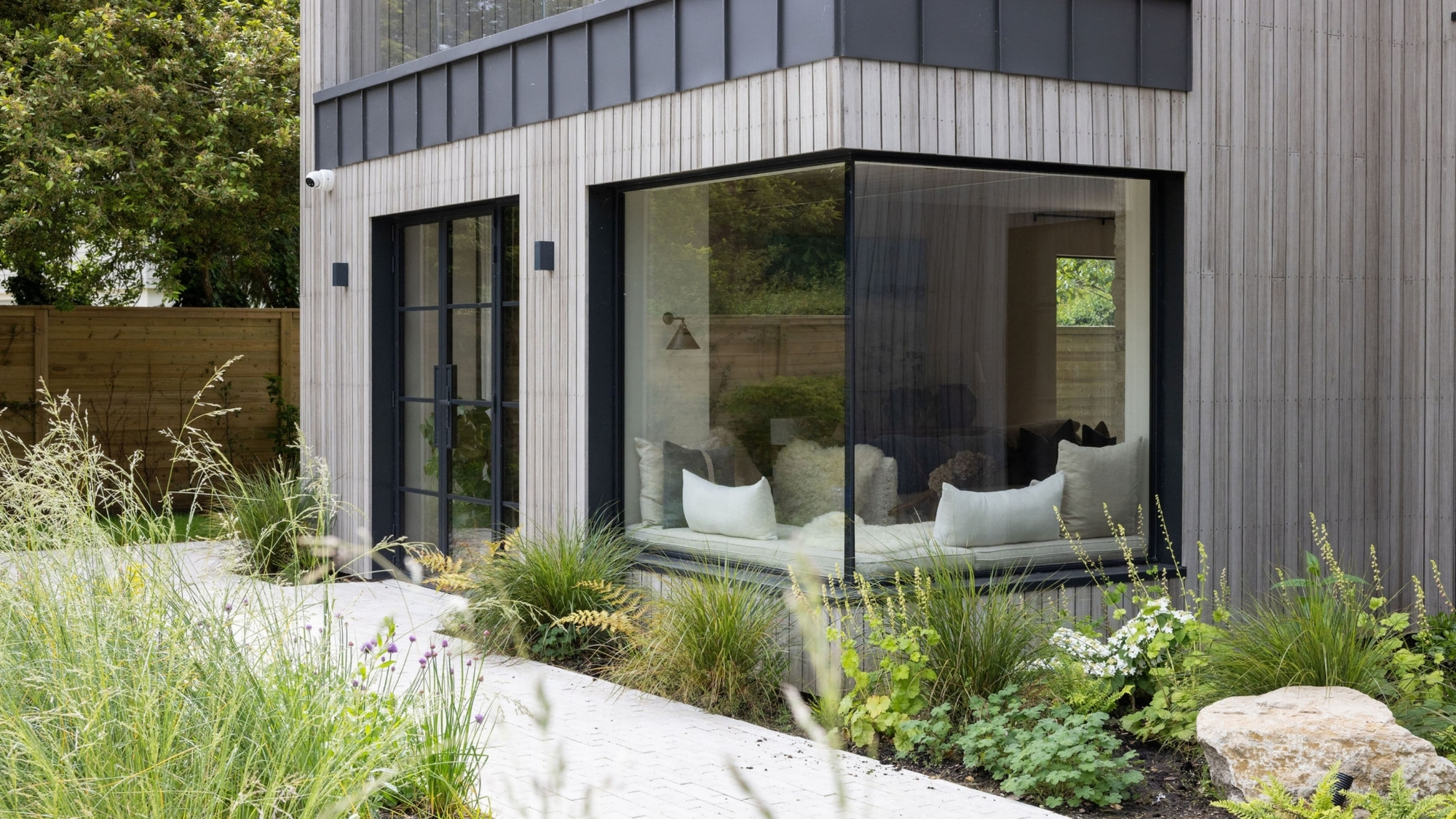 Timber-clad house extension with a glass corner window seat, sliding doors, and a landscaped garden.