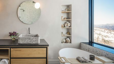 A spa-like bathroom with a mirror and lighting on the mirror. There is a large window welcoming in natural light.