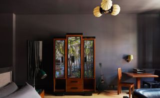 Interior view of a room at Ace Hotel, New Orleans, US featuring dark coloured walls, a bed, a wall-mounted mirror, a wooden wardrobe with a tree design, a black guitar, a wooden table and a wooden chair