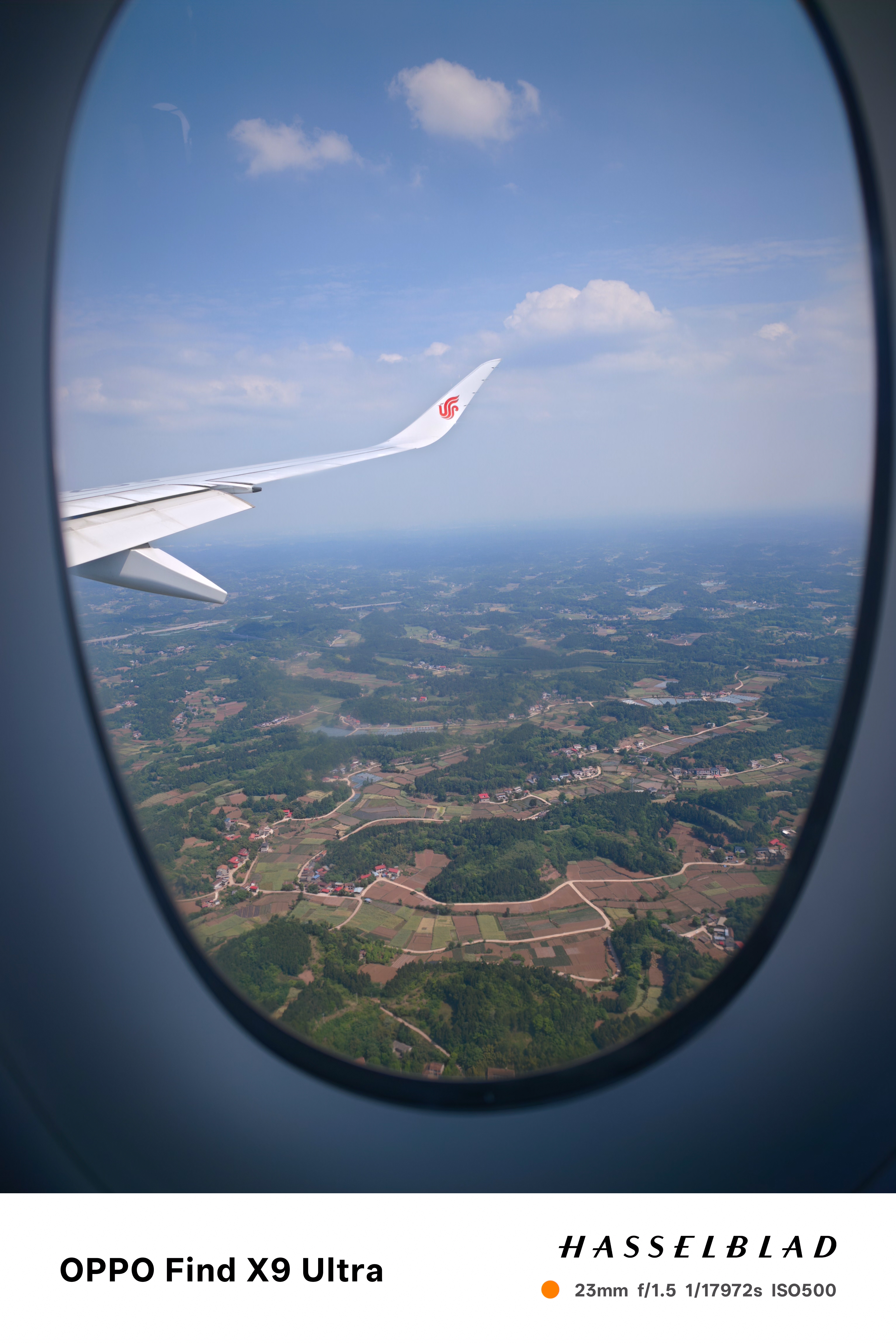 View from an airplane window showing wing, clouds, and fields below