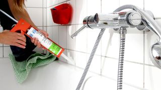 Person applying silicone with caulking gun to white bath and tiles