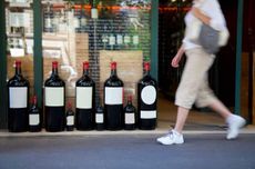 Person walking past shop with large wine format bottles in window