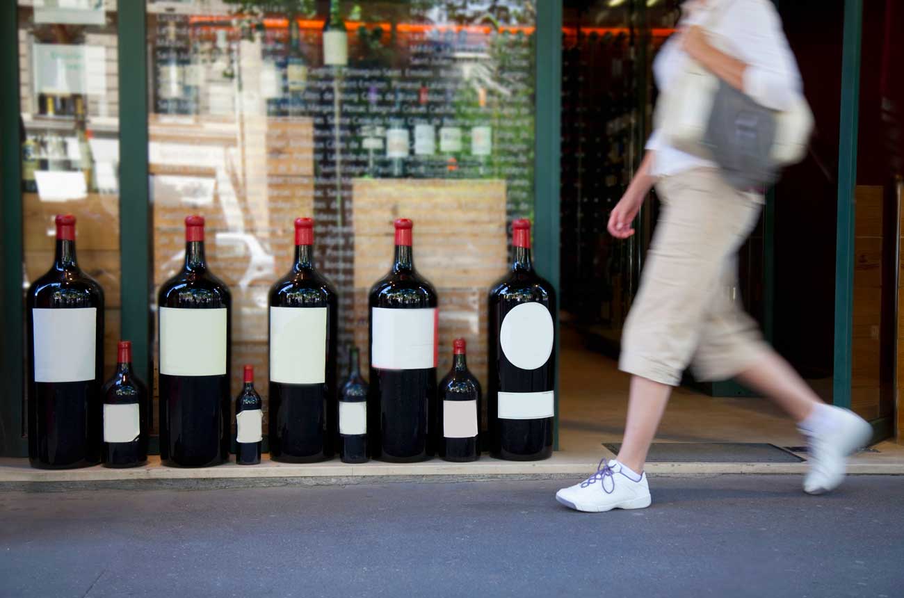 Person walking past shop with large wine format bottles in window