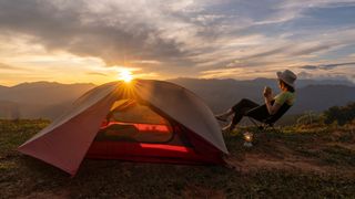 Woman sitting outside tent at sunrise looking out across mountains