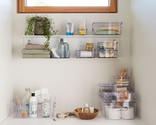 Bathroom shelves with stackable containers, glass bottles, towels and a plant above a bathroom counter from ORTHEX
