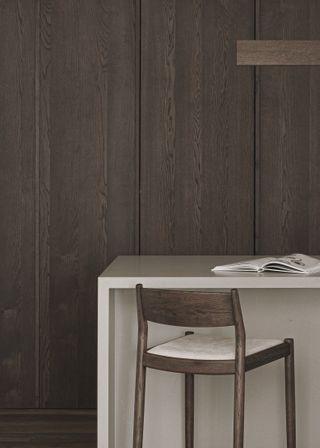 Tall desk in stone and bar stool in wood photographed in front of a wood panelled wall