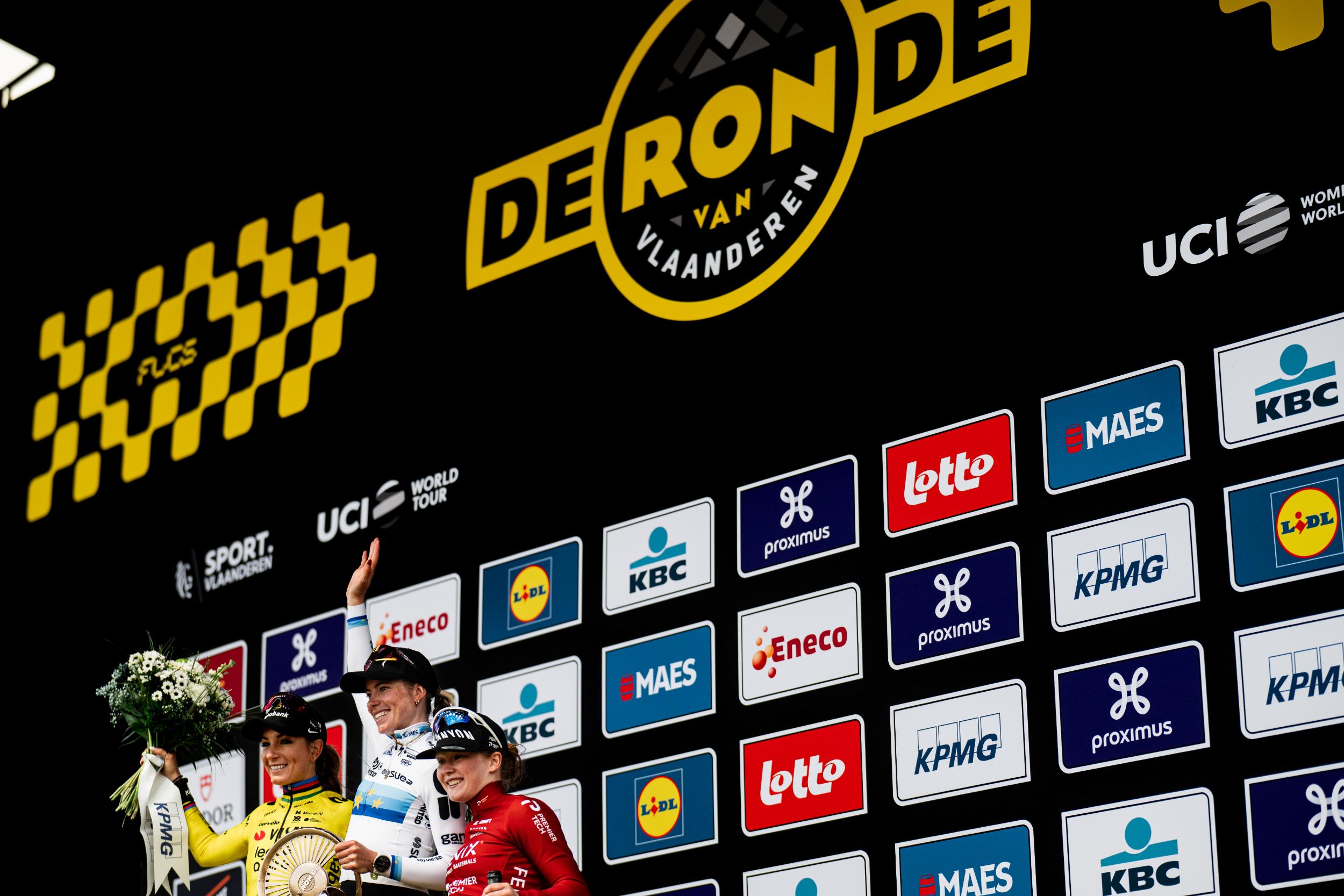 The podium finishers in front of an advertising board at the Tour of Flanders Women 2026