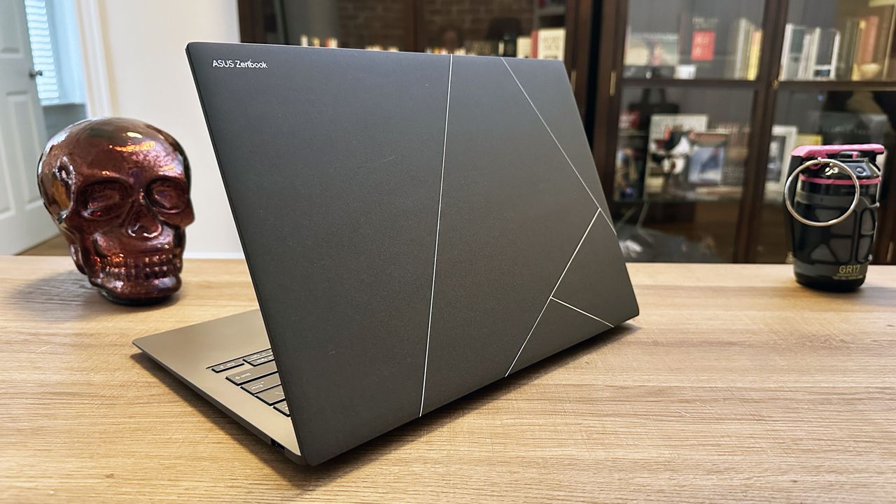 Asus Zenbook S 14 open on a wooden desk angled slightly away from camera showing the stylized Asus logo on the lid.
