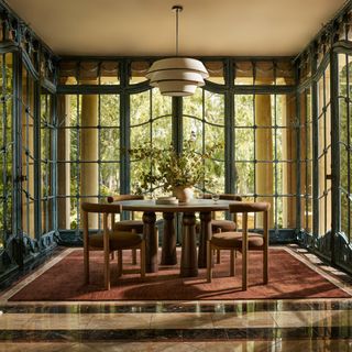 A dining room with floor-to-ceiling windows and a white and black light fixture hanging above a circular table