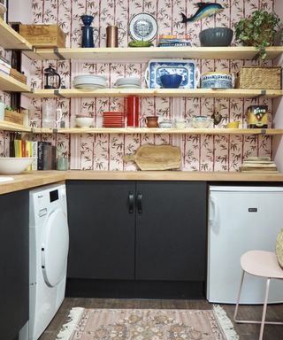 A laundry room with wooden shelves and pink printed floral wallpaper