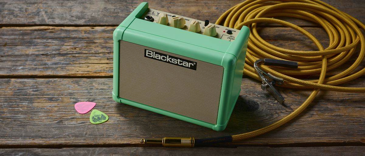 A Blackstar Fly 3 guitar amp on a wooden floor with guitar picks and cable