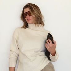 Sofia wears oversize sunglasses, a white turtleneck sweater, and a clutch.