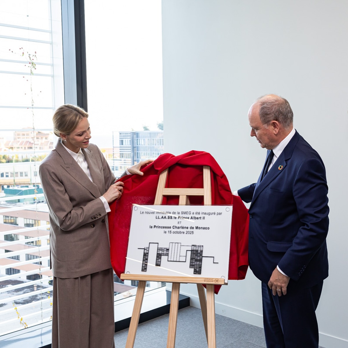 Princess Charlene and Prince Albert wearing suits and unveiling a plaque