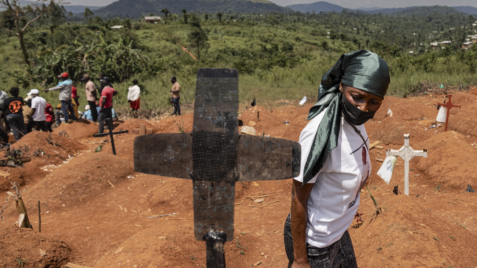  A woman wearing a mask walks by a grave marker with other people in the background