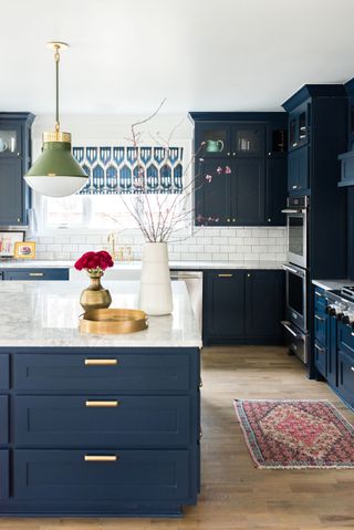 navy blue kitchen with green and white pendant light white worktops and backsplash and persian style rug