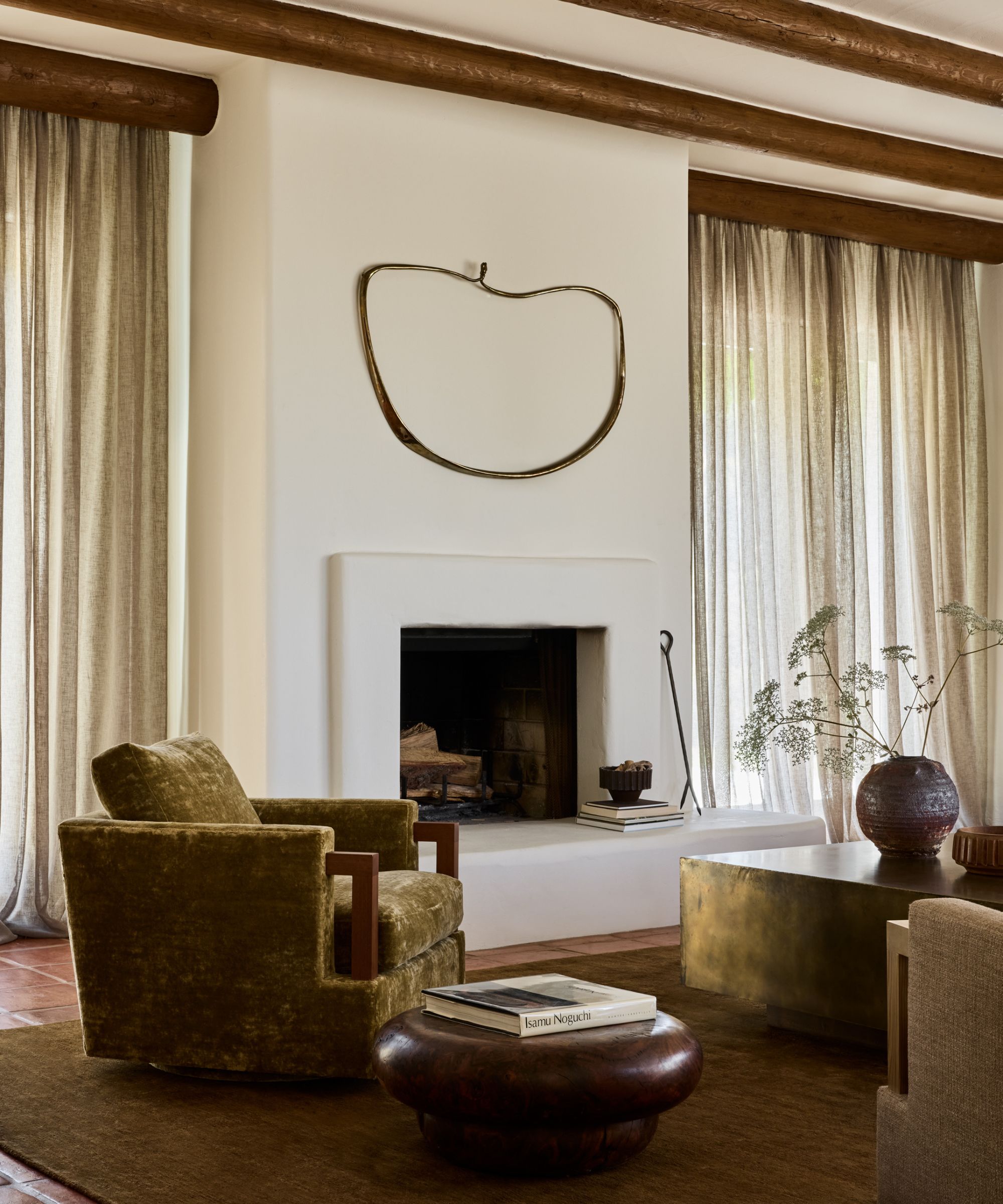 An adobe home living room with white plastered walls, earthy green armchair and a round wooden side table