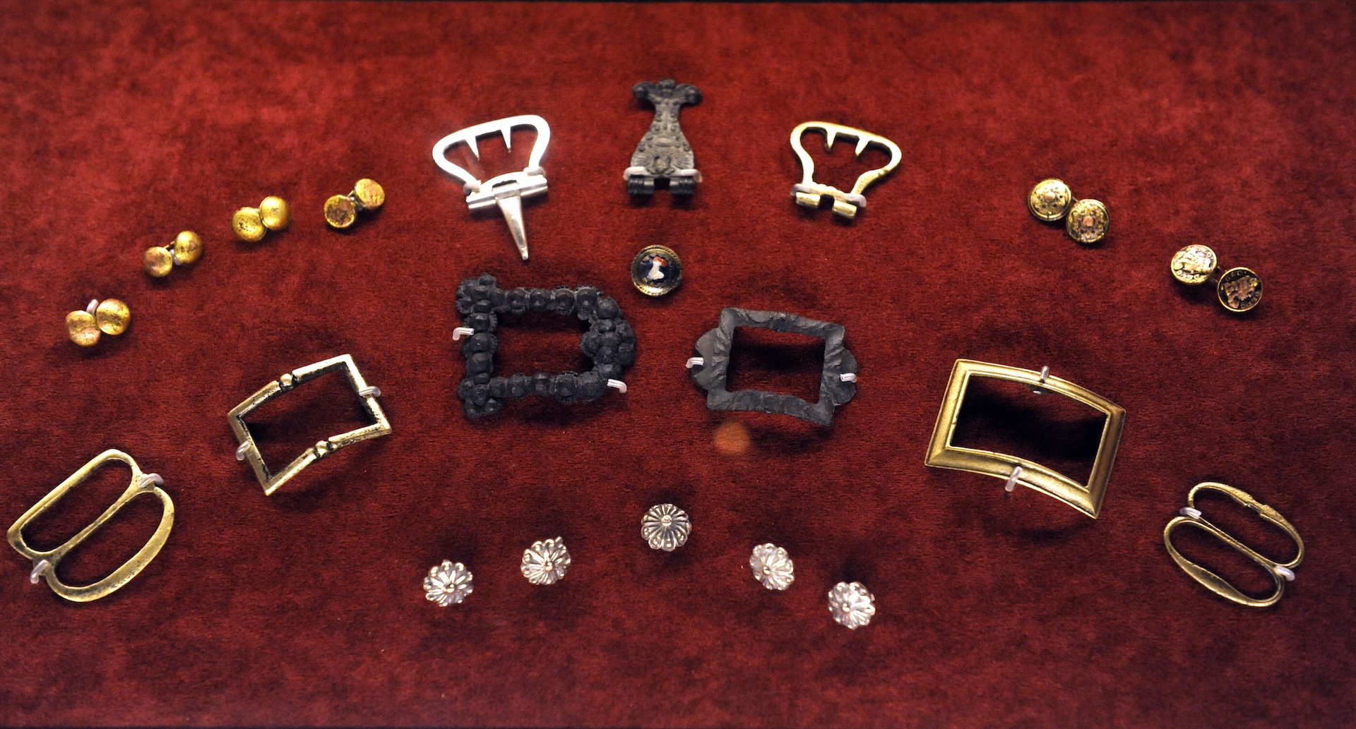 a collection of belt buckles, cufflinks, and buttons laid out on red velvet