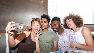 A group of friends sit together in a restaurant and pose for a selfie photo.