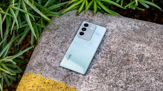 Vivo V27 lying face down on a cement block surrounded by leaves