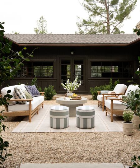 mcgee & co outdoor living room in a shingled courtyard with wooden sofas facing each other on a striped rug with two small green and white striped ottomans
