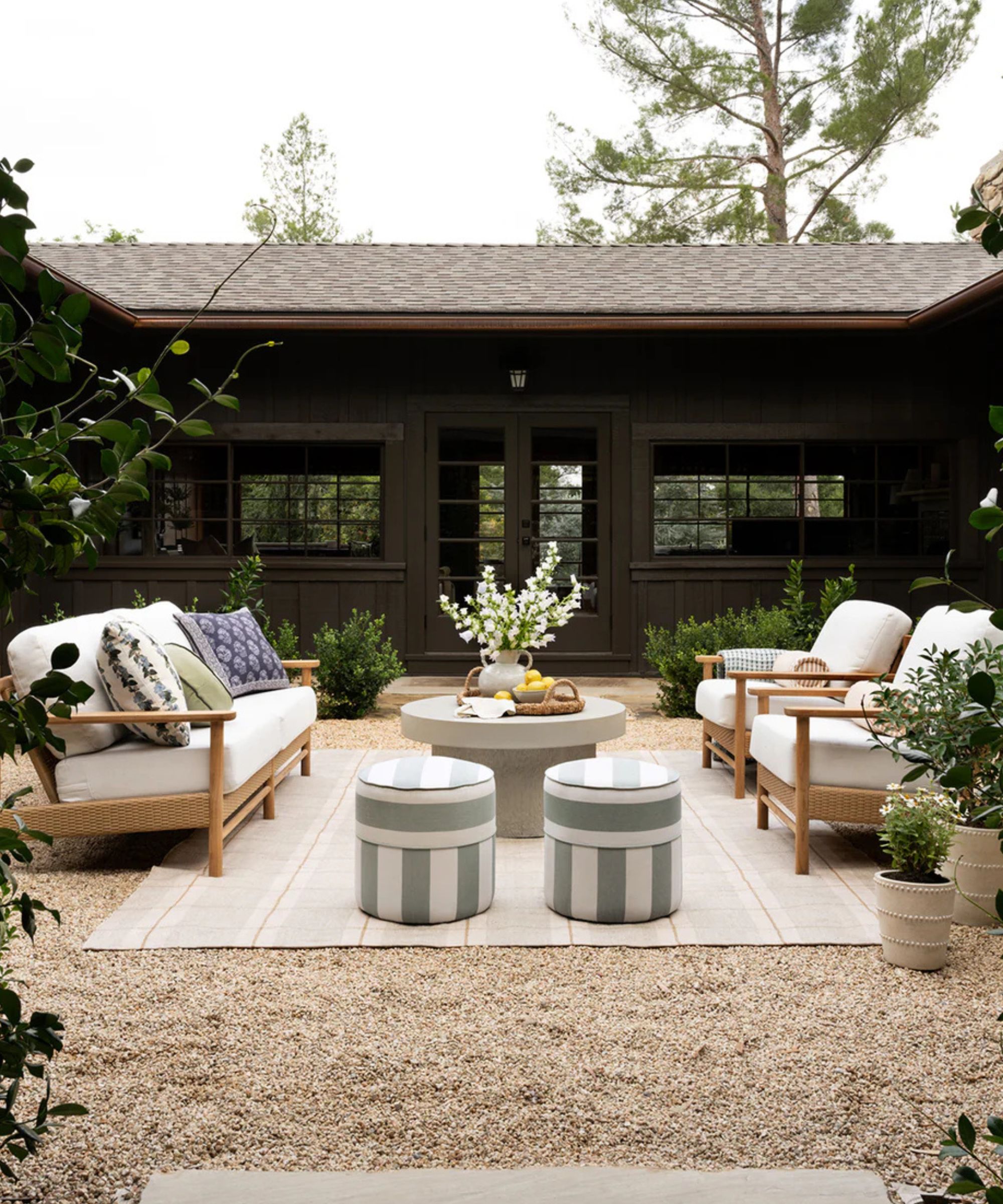 mcgee & co outdoor living room in a shingled courtyard with wooden sofas facing each other on a striped rug with two small green and white striped ottomans