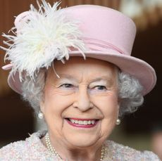  Queen Elizabeth smiling and wearing a pink hat and coat with pearl earrings