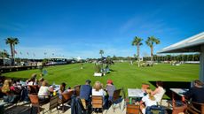 Spectators watch a horse jump a showjump on a grass arena againstva bight blue sky at the Sunshine Tour