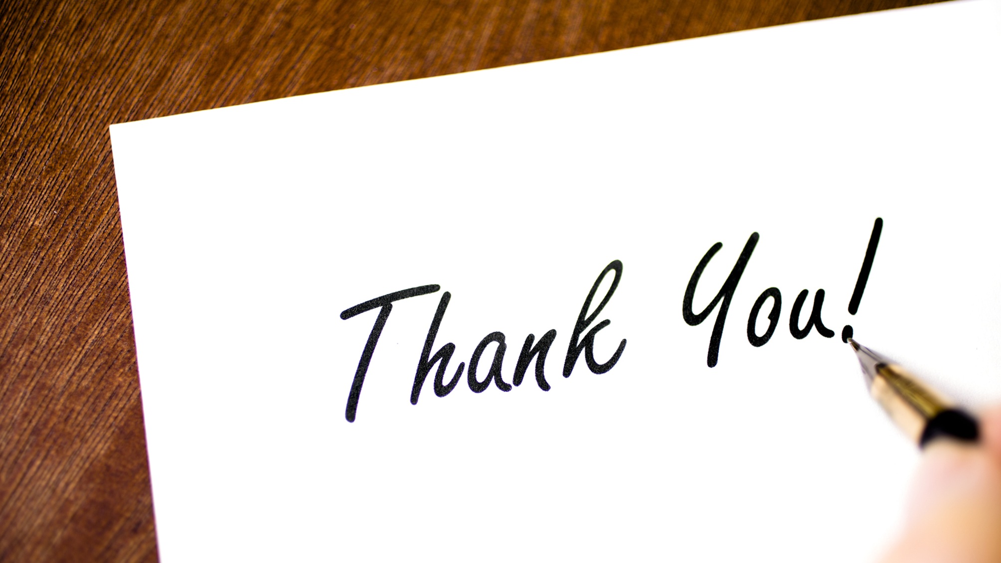 A fountain pen writing the words &amp;quot;thank you,&amp;quot; only the writer's fingers showing.