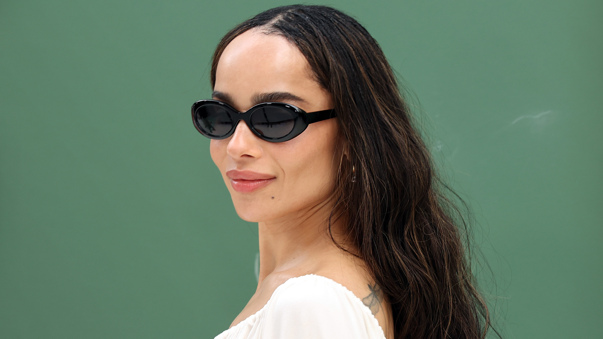 Zoe Kravitz in front of a blank wall wearing sunglasses