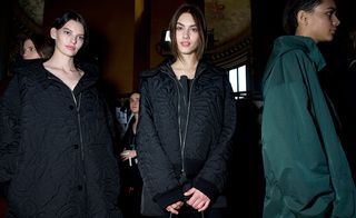 Two models in black coats and one in a dark green coat