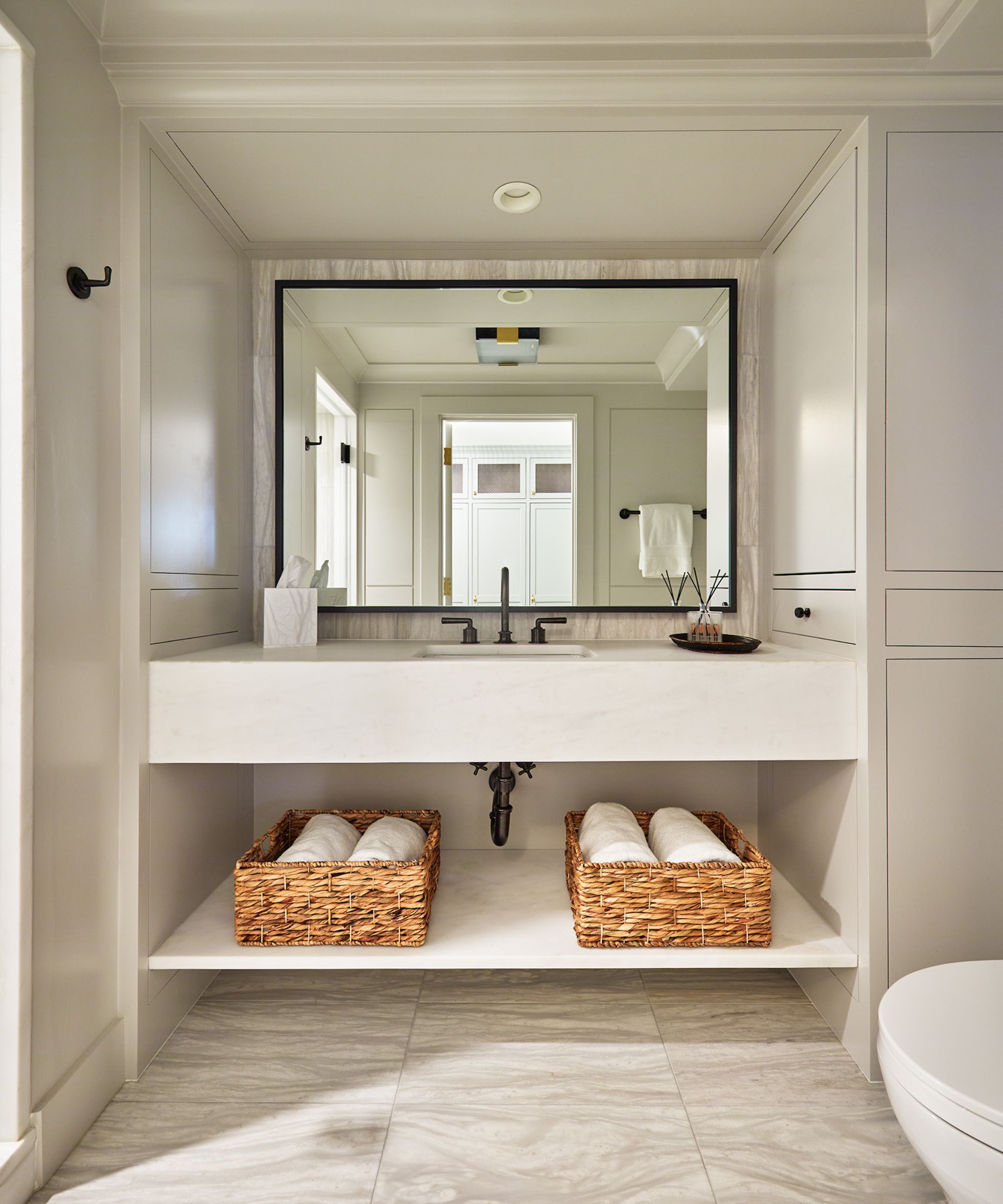 A minimalist bathroom with white walls, a black vanity mirror, and light wooden paneling