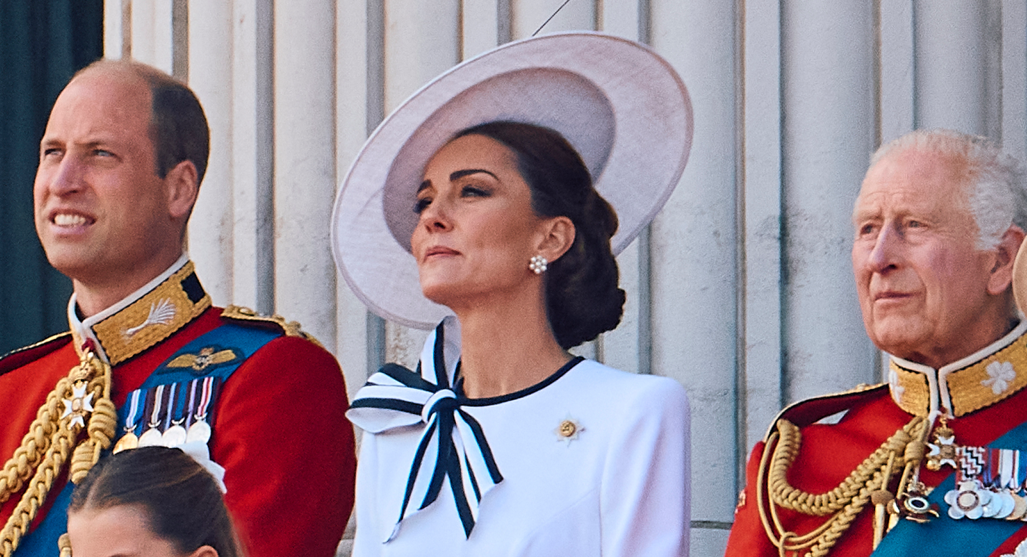 Prince William and King Charles wear military uniform as they stand on the Buckingham Palace balcony with Kate Middleton, who wears a white dress with navy accents