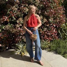 Woman wears red halter top, blue barrel-leg jeans, and carries woven raffia bag