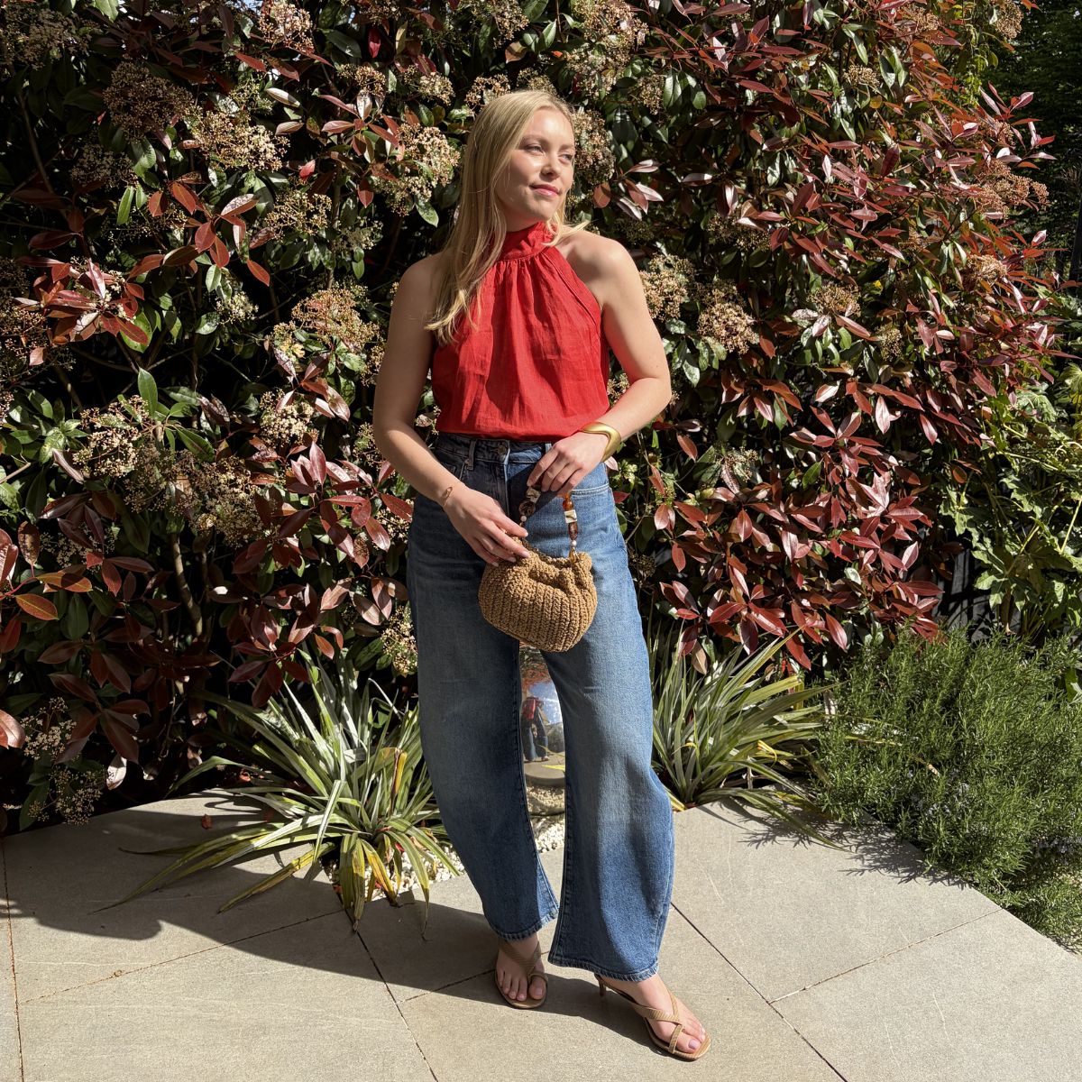 Woman wears red halter top, blue barrel-leg jeans, and carries woven raffia bag
