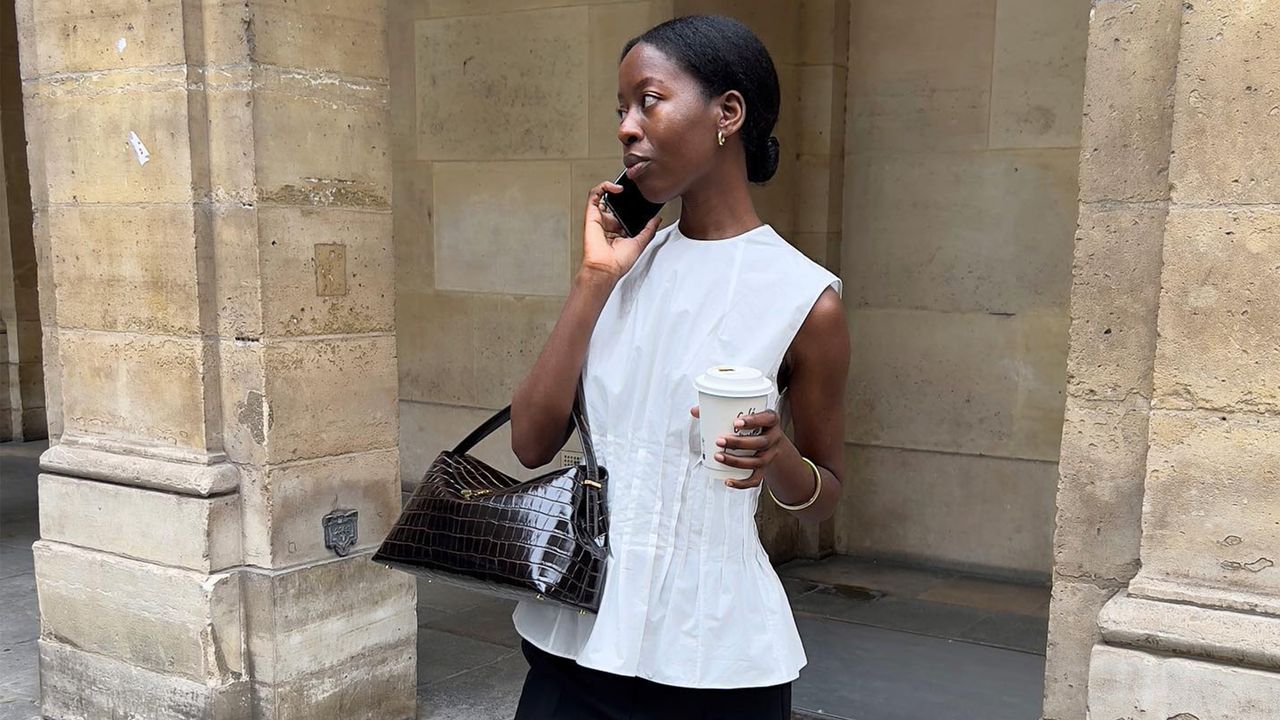 Sylvie Mus talking on the phone wearing a white peplum top with a brown croc-effect Toteme T-Lock handbag.