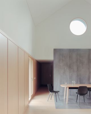 White dining room with wood panelled walls, grey zoned area for dining table and chairs, and porthole window up high