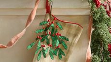 Beaded tree branch charm hanging off of gingham Christmas stocking on a neutral fireplace mantel