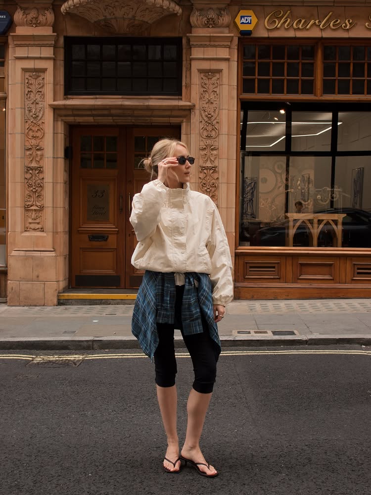 An image of @chloekathbutler wearing a white windbreaker, black capri leggings and a checked shirt that&#039;s tied at the waist.