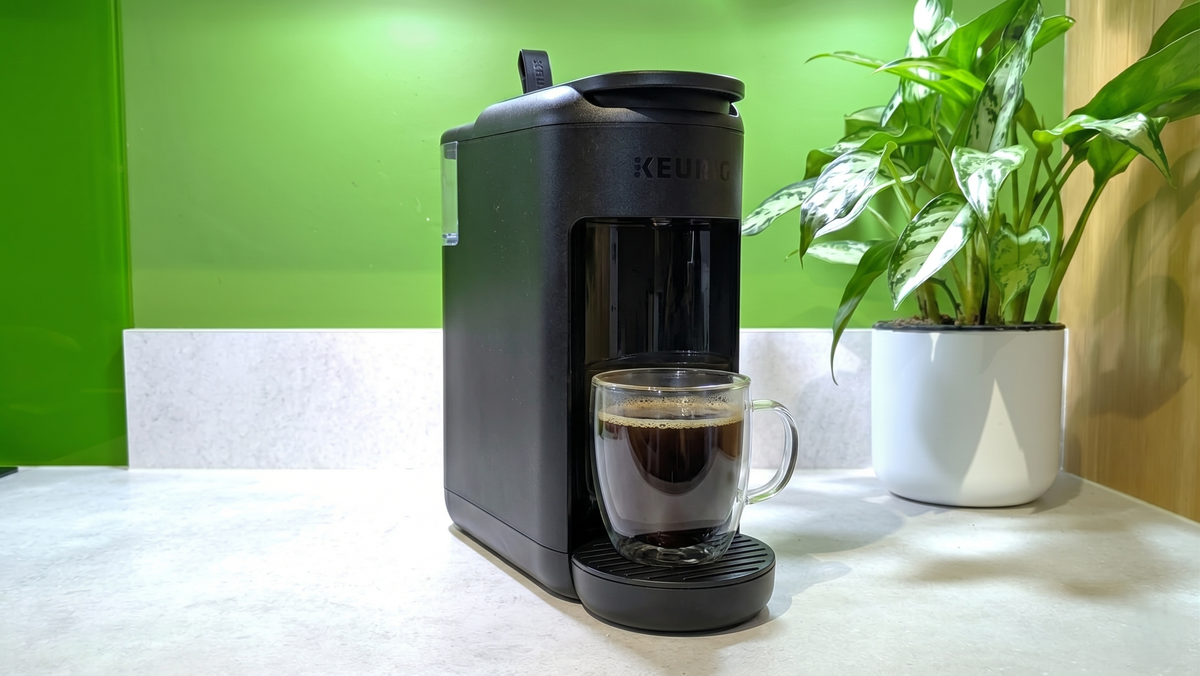 Keurig K-Mini Mate coffee maker on light gray kitchen counter with cup of coffee and a plant
