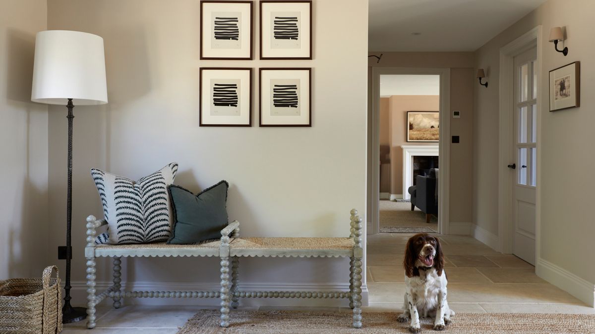 neutral coloured hallway idea with floor lamp, black and white artwork, bench seat and brown and white spaniel dog sat on hallway runner on top of tiled floor