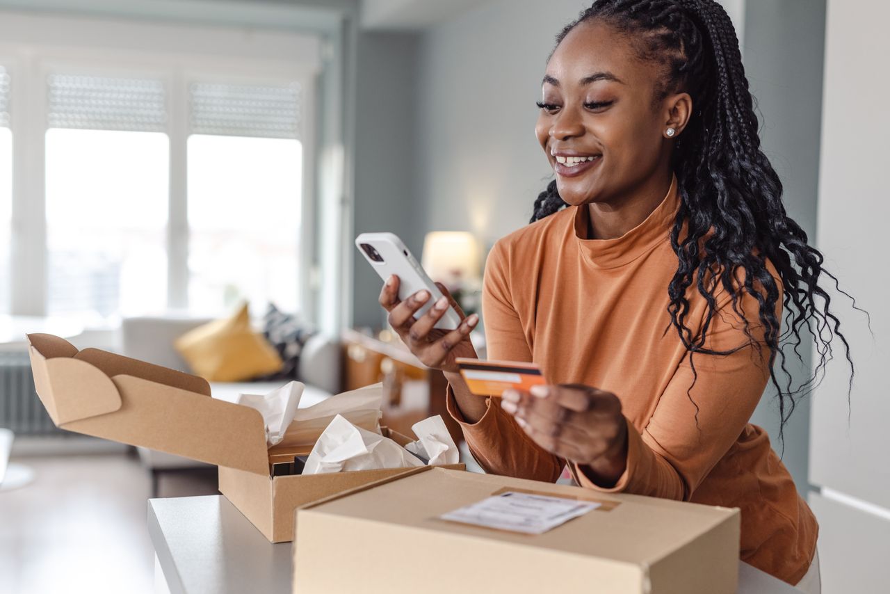 Woman shops online with a credit card next to boxes on counter.